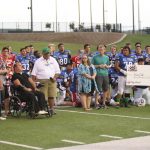 Group photo of both teams and beneficiaries on the field.